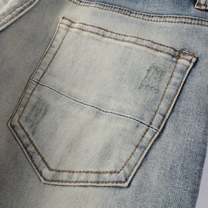 Gros plan de la poche arrière en jean délavé bleu clair avec coutures et broderie lettrée