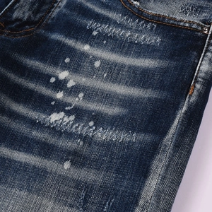 Detailed macro view of dark blue jeans featuring distressed holes and white paint splashes