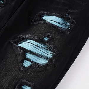 Macro detail of men's black distressed jeans with blue ribbed fabric patch and frayed edges