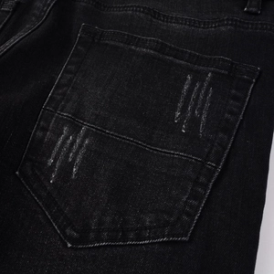 Macro view of men's black distressed denim jeans showing back pocket stitching and fabric