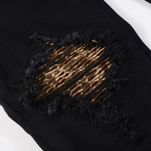 Macro detail of distressed black jeans featuring golden pleated patchwork and frayed edges