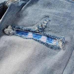 Macro shot of light blue denim jeans showing ripped details and plaid inner patch