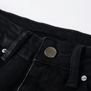 Close-up of black denim waist with silver metal button and reinforced stitching detail