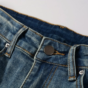 Macro detail of washed blue denim jeans waist with metal button and orange stitching