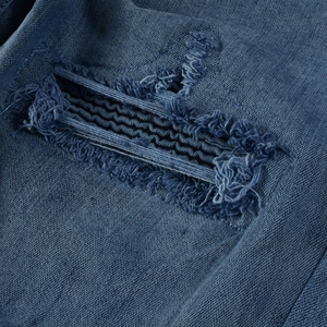 Gros plan sur denim bleu délavé avec bords effilochés et coutures décoratives noires