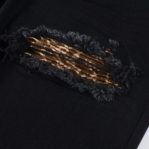 Detail shot of black denim distressed jeans featuring leopard print patches and frayed edges