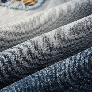 Macro detail of washed blue denim fabric featuring a distressed hole and plaid patch
