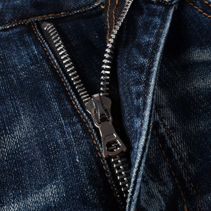 Close-up of metal zipper and yellow contrast stitching on dark blue slim-fit denim jeans
