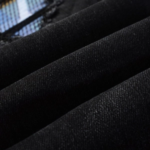 Close-up of black denim fabric texture with distressed ripped detail and blue mesh patch