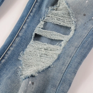 Detail of ripped jeans featuring blue patches, paint splatters, and heavy distressing