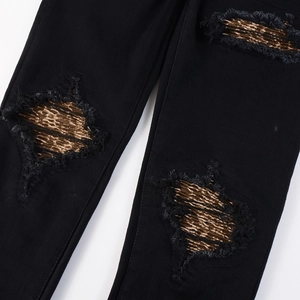Detail view of black distressed jeans featuring leopard print patches and frayed edges