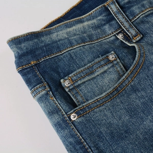 Detail of blue wash denim jeans showing yellow contrast stitching and silver metal rivets