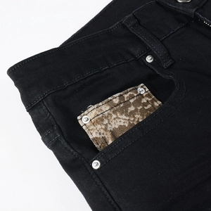 Detail of black jeans featuring silver studs and leopard print patch on front pocket