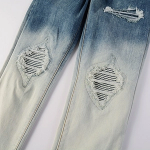 Detail of distressed ripped denim jeans with blue cross-stitch patch and faded wash