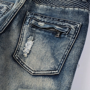 Detail of distressed blue jeans featuring a zippered back pocket and horizontal pleats
