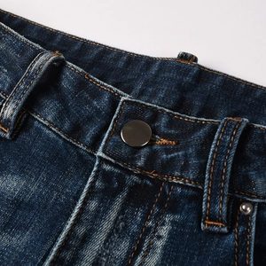 Detailed close-up of dark blue denim jeans with metal button and orange contrast stitching