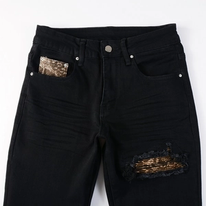 Detail of black slim jeans featuring ripped holes with metallic fabric patchwork and silver button