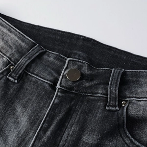 Détail de la taille en jean noir délavé avec moustaches et bouton métallique