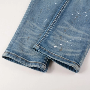 Close-up of distressed blue denim hem with paint splatter detail and heavy wash finish