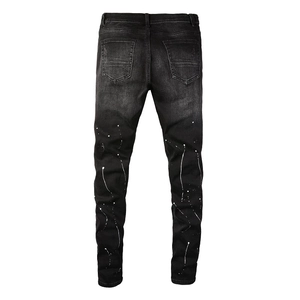 Detail view of black slim denim jeans with white paint splatter and distressed back pocket