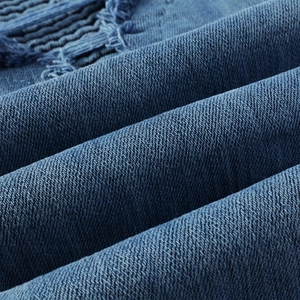 Gros plan sur le tissu denim bleu avec texture sergé et détails d'ourlets effilochés