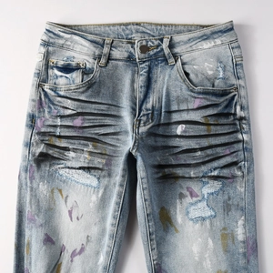 Détail d'un jean bleu délavé avec des taches de peinture colorées et des déchirures usées
