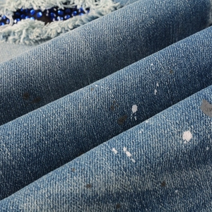 Detail of dark blue denim jeans with paint splatters, distressed holes, and blue rhinestones