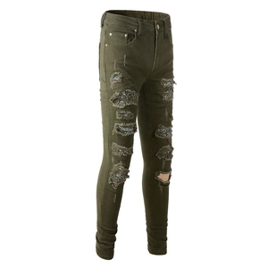 Dettaglio dei jeans strappati verde militare con patchwork argento metallico e usurati