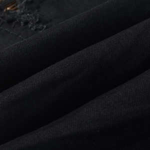 Macro shot of black denim fabric detailing distressed holes and leopard print patches