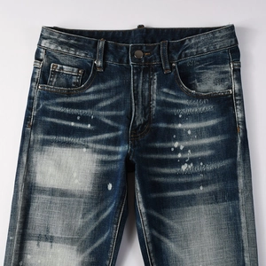 Dettaglio di jeans blu scuro con effetto baffi di gatto e schizzi di vernice vintage