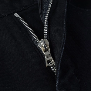 Detail shot of the silver metal zipper and reinforced stitching on black denim pants