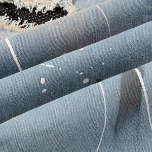Macro shot of light blue denim with white stripes, splatter paint, and sequin embroidery details