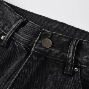 Close-up of vintage washed black denim waist with matte silver button and detailed stitching