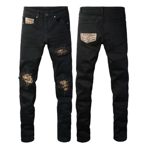 Close-up of black slim fit jeans with distressed holes and gold snakeskin patches