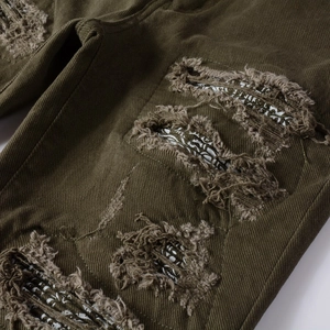 Dettaglio del denim verde oliva invecchiato con fori sfilacciati e toppe in tessuto paisley