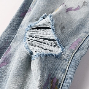 Détails rapprochés du jean bleu avec taches de peinture violettes et effet déchiré