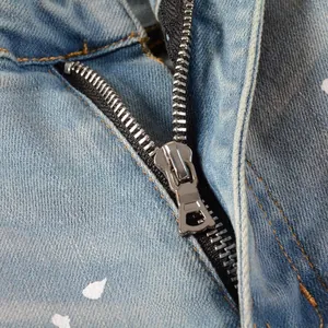 Detail of metal zipper fly on light blue distressed denim with white paint splatter