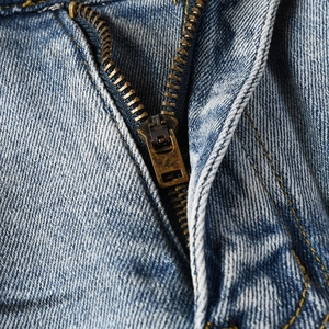 Macro view of bronze metal zipper and contrast stitching on washed denim jeans