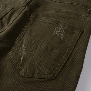 Dettaglio della tasca posteriore dei jeans verde militare con fori logori e trama twill