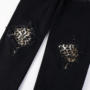 Close-up of black denim jeans with distressed knee holes and leopard print patches