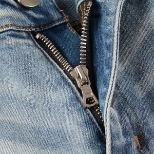 Detailed macro view of the silver metal zipper and durable orange stitching on blue denim