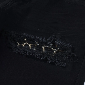 Macro shot of distressed black denim with leopard print patch and frayed edges details