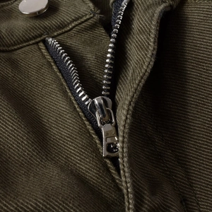 Dettaglio della cerniera in metallo e del bottone sui pantaloni denim verde militare