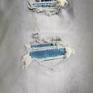 Close-up of distressed light blue denim jeans featuring heavy ripping and blue rhinestones