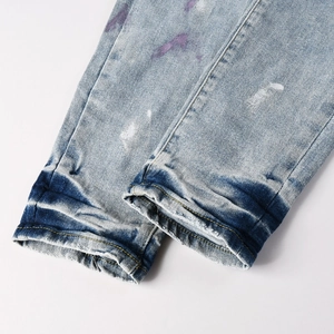 Detail of ripped blue jeans featuring white and purple paint splatter and distressed hem