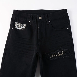 Detail view of black distressed jeans featuring leopard print patches and metal chain accents