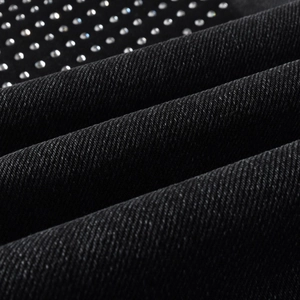 Detail of black denim fabric with rows of sparkling silver rhinestones and stud rivets