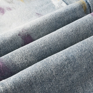 Close-up of heavy-duty light blue denim fabric with artistic purple and yellow spray paint