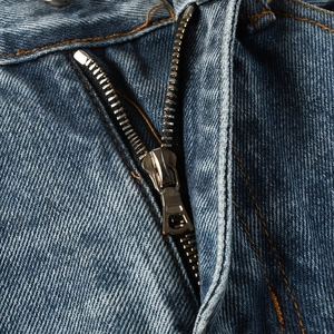 Detailed close-up of metallic zipper and orange contrast stitching on dark blue denim jeans