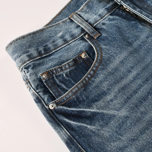 Detailed macro view of denim jeans waist with metal rivets and yellow contrast stitching